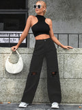Women's high waist casual ripped jeans in black outfit with white bag against a stone wall
