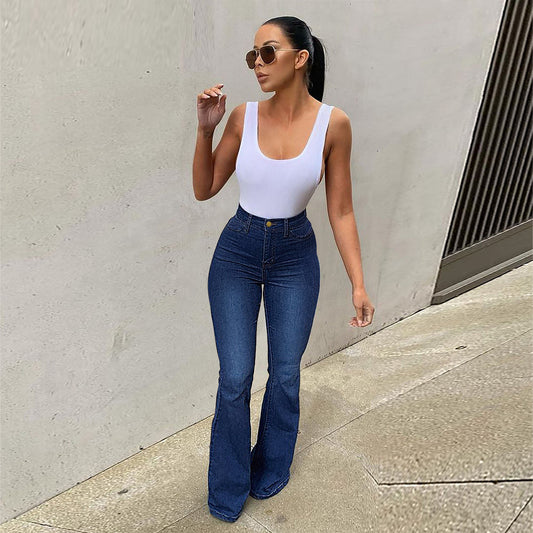Woman wearing blue high-waisted stretch bootcut jeans and white top standing against light gray wall
