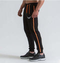 Person wearing black jogger pants with orange accents on a white background