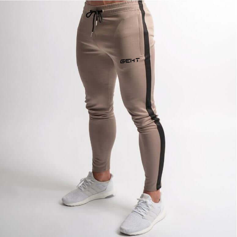 Beige jogger pants with black side stripe and 'GEHT' branding on a white background
