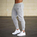 Person wearing gray jogger pants with a logo and white sneakers on a blurred background