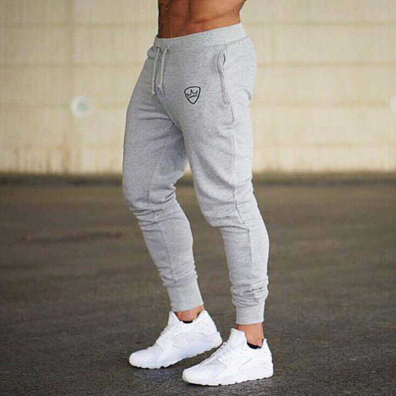 Person wearing gray jogger pants with a logo and white sneakers on a blurred background