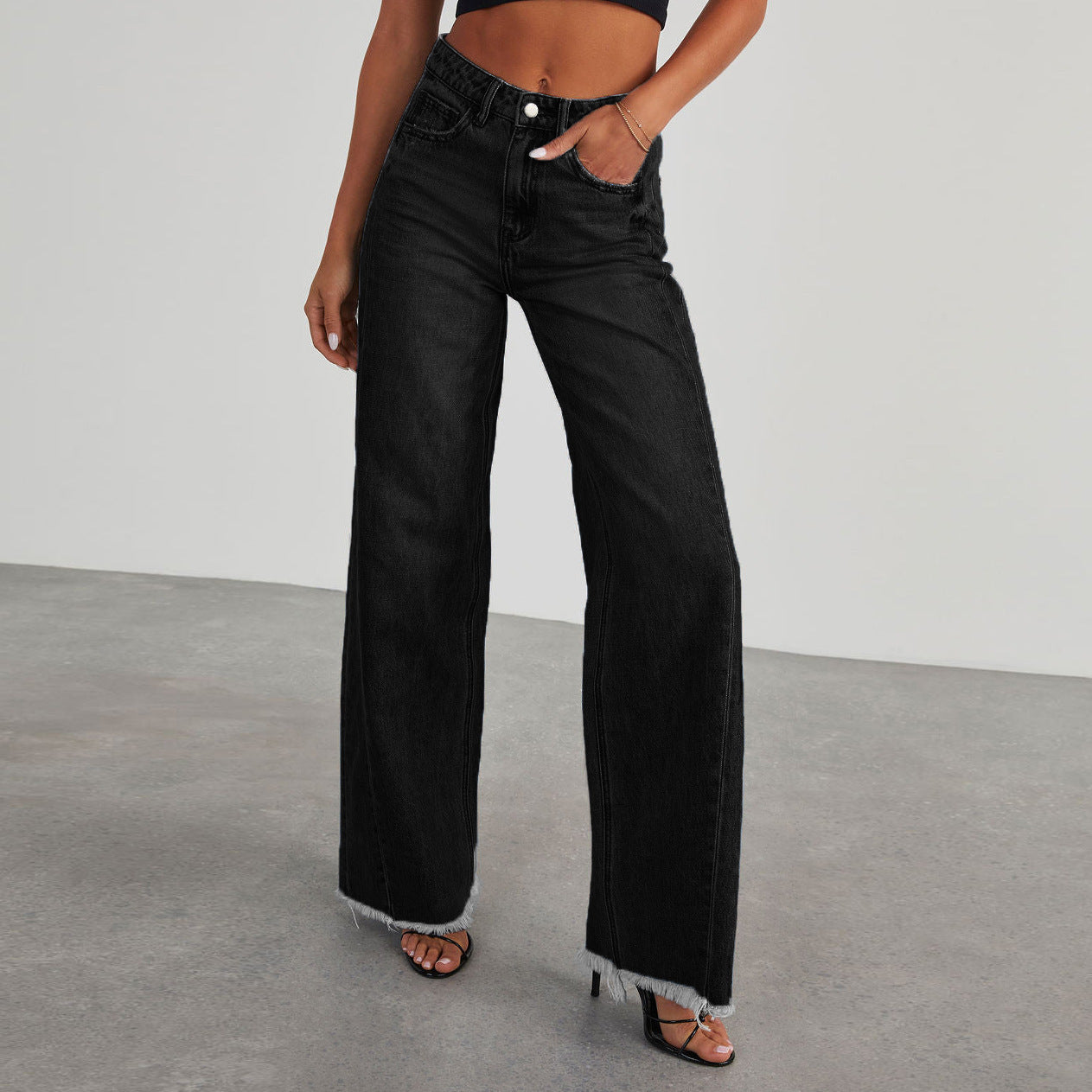 Person wearing black wide leg jeans with a straight leg design on a plain background.