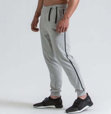 Person wearing gray jogger pants with black drawstrings and side stripes on a white background