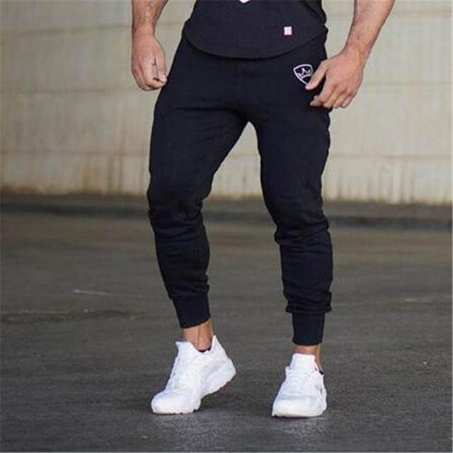 Person wearing black jogger pants and white sneakers on a concrete surface.