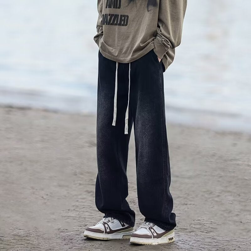 Man wearing black pants and a beige sweatshirt with text on it, standing on a beach.