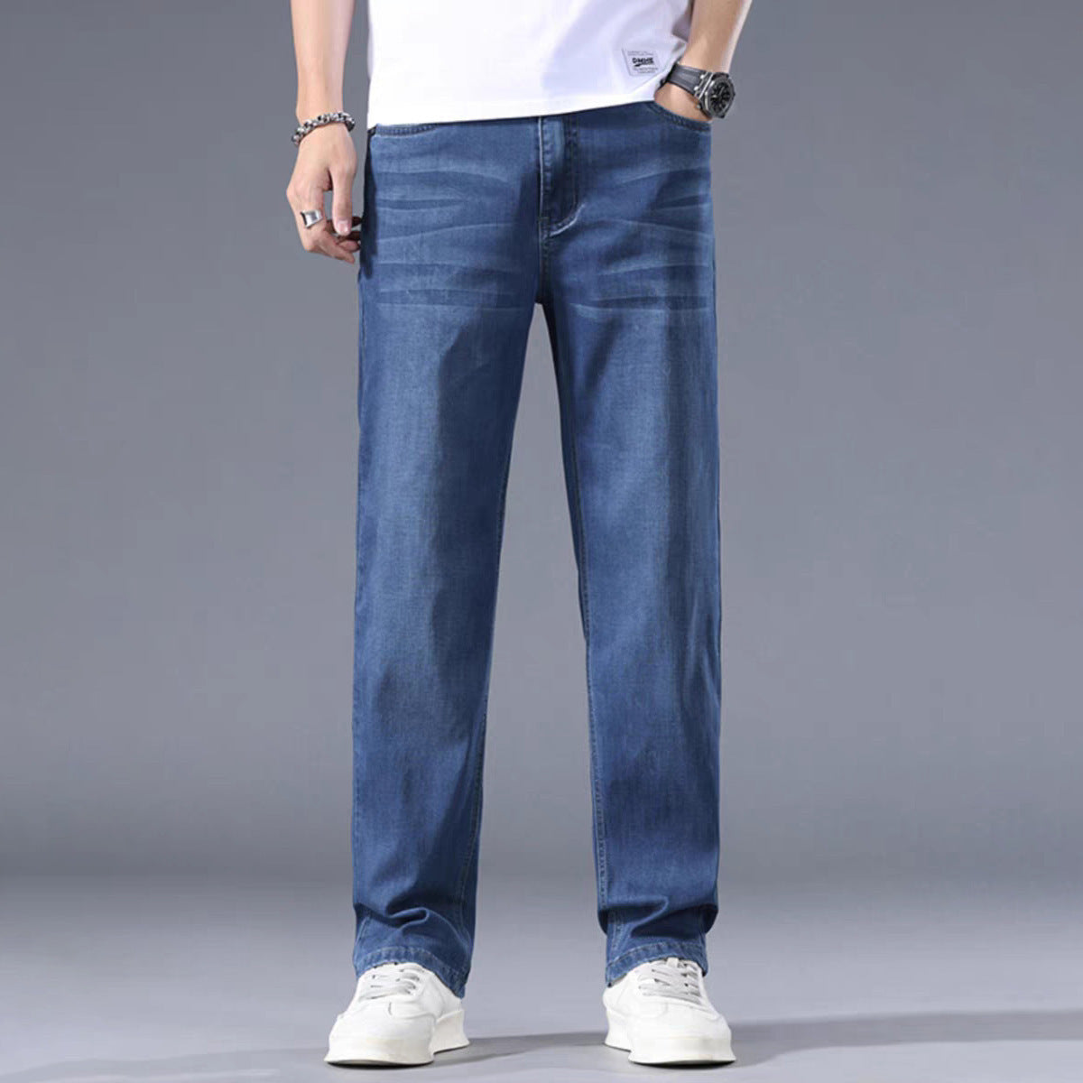 Person wearing blue jeans and white sneakers on a gray background