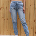 Woman wearing light blue wide-leg elastic waist jeans standing against a wooden fence background