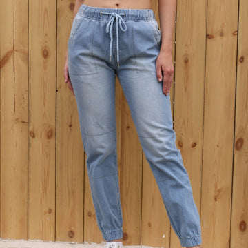 Woman wearing light blue wide-leg elastic waist jeans standing against a wooden fence background
