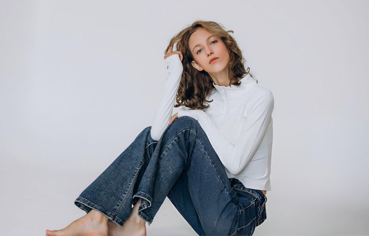 Woman wearing a white sweater and blue jeans sitting on a white background - JeansSpot 