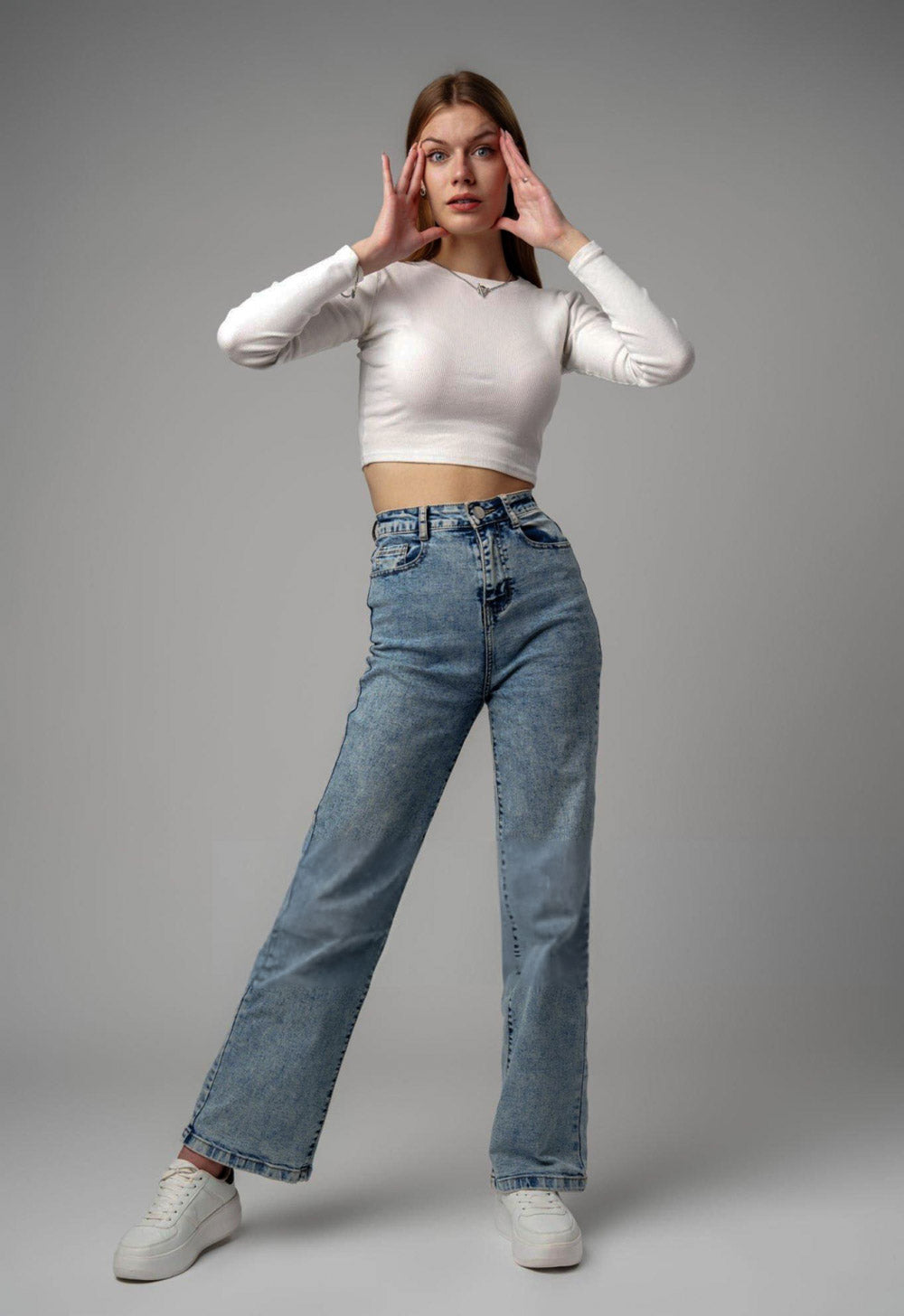 Woman wearing a white long-sleeve top and blue jeans on a gray background - JeansSpot 