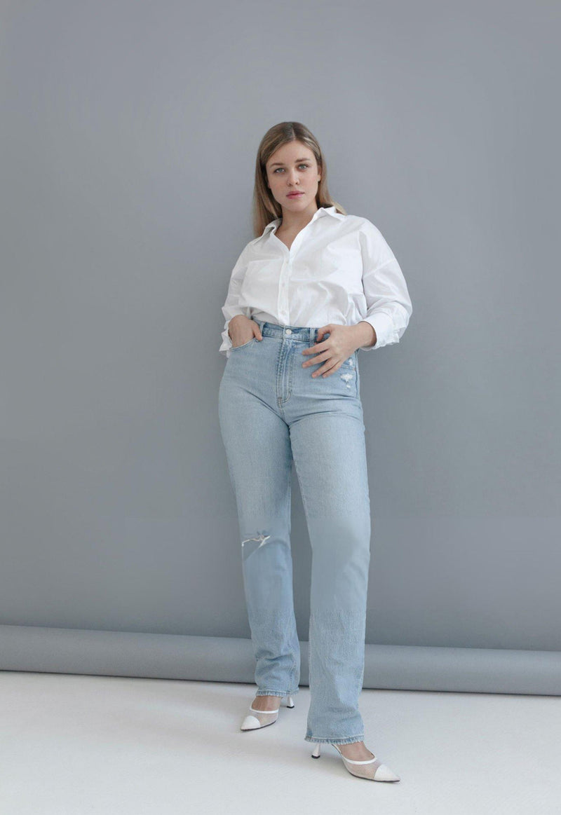 Woman wearing a white shirt and light blue jeans against a gray background - JeansSpot 