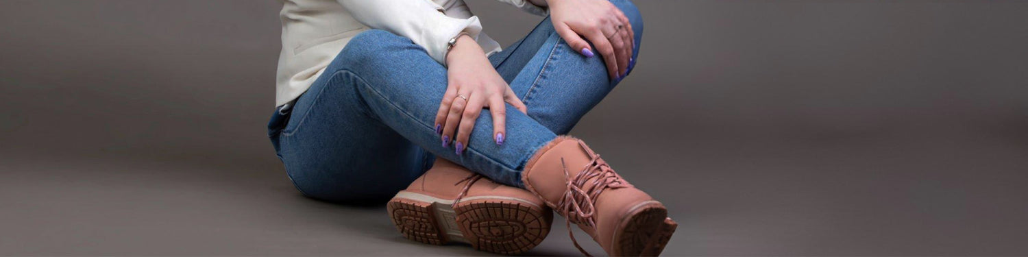 Person wearing blue jeans and brown boots sitting on a gray background - JeansSpot