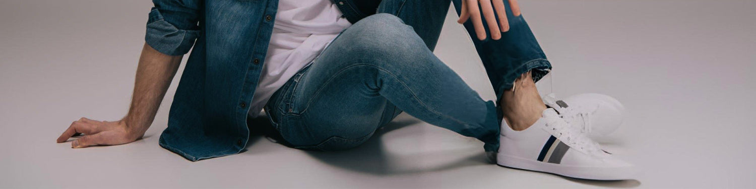Person wearing blue jeans and white sneakers sitting on a light gray background - JeansSpot 