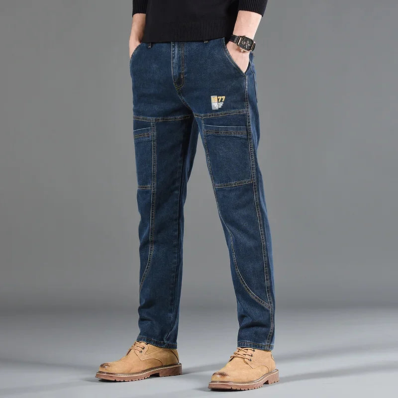 Man wearing straight cut blue six-pocket casual jeans with brown shoes on a gray background