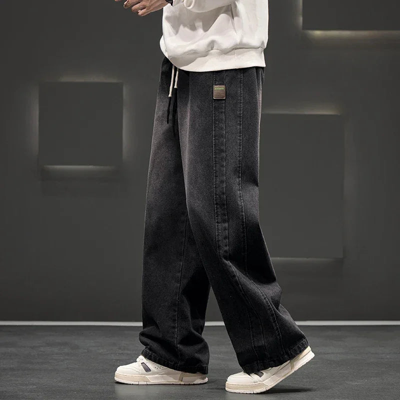 Man wearing dark wide-leg loose straight fit denim jeans with a white shirt against a gray background