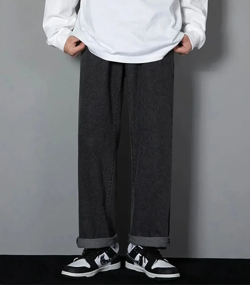 Person wearing a white sweatshirt and dark gray wide-leg pants with black and white sneakers on a plain background