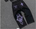 Black jeans with white embroidered designs on a gray surface