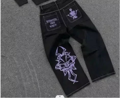 Black jeans with white embroidered designs on a gray surface