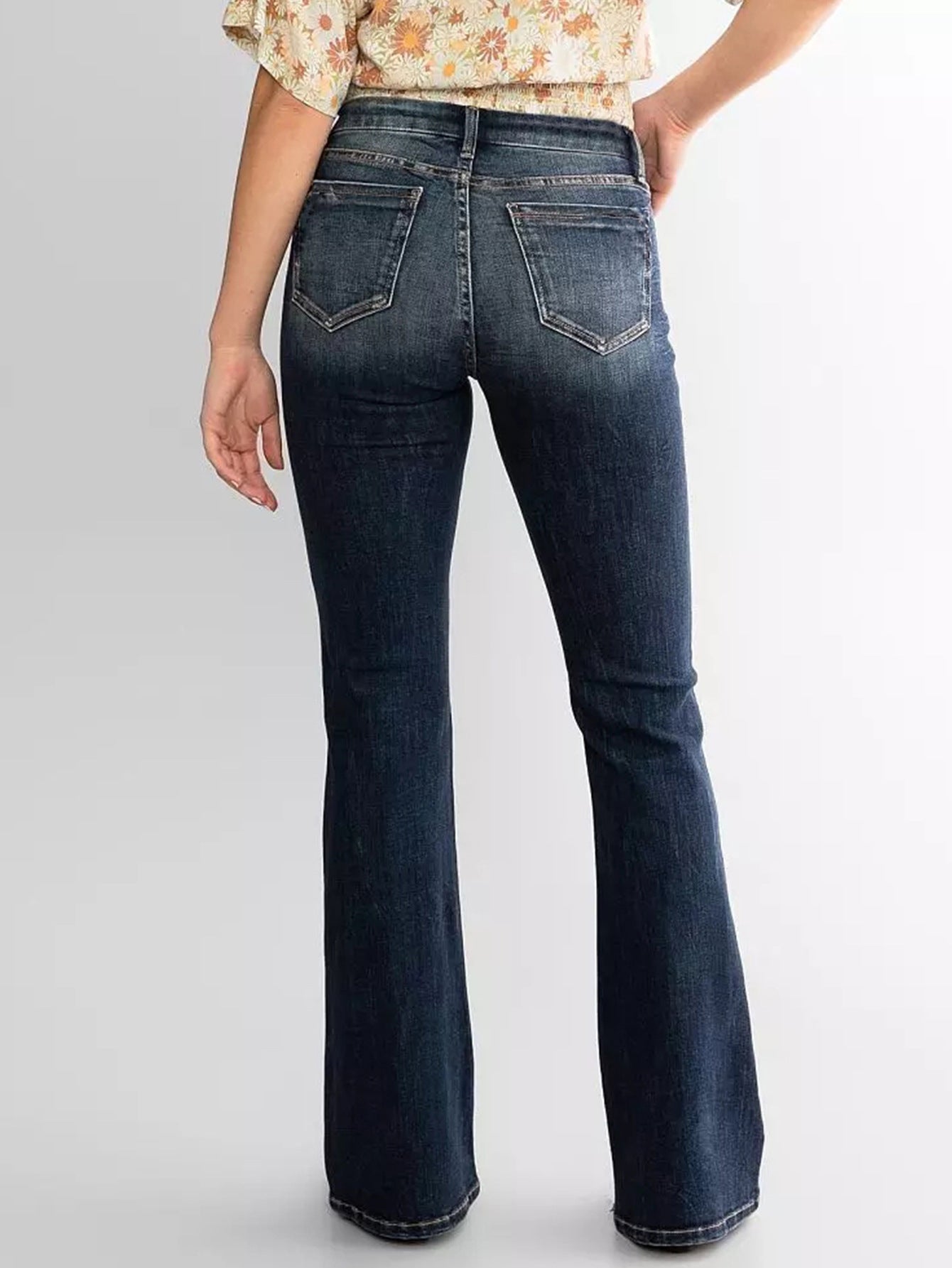 Woman wearing blue mid waist slim fit flared jeans on a plain background – JeansSpot