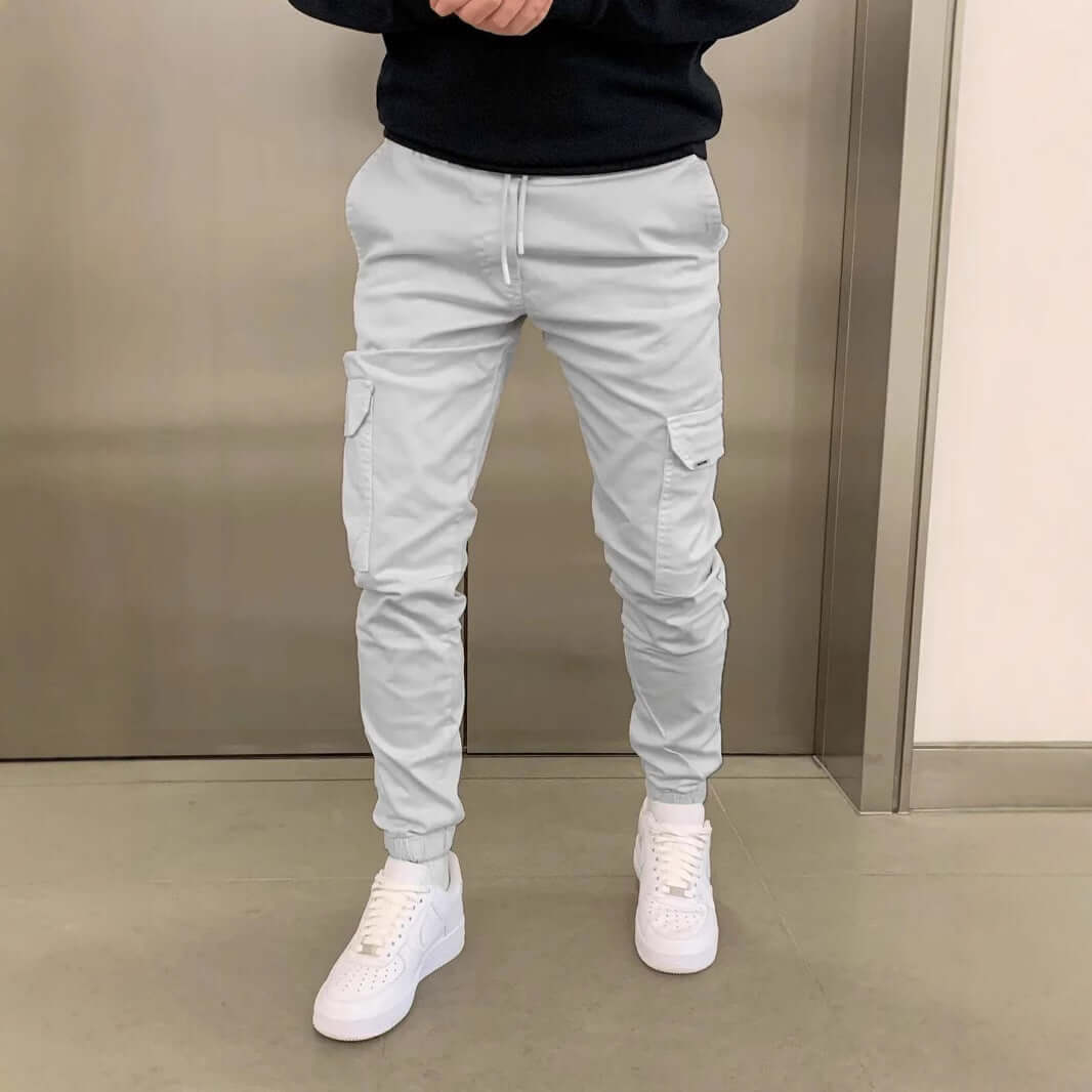 Man wearing light gray cargo jogger pants with white sneakers on a neutral background